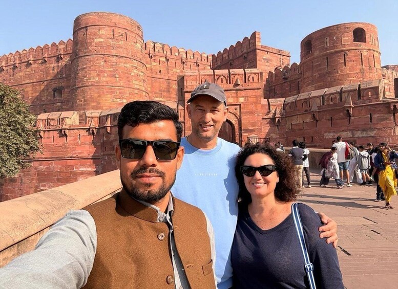 A group of people taking a selfie in front of a historic fort with red brick walls and arched windows. 4