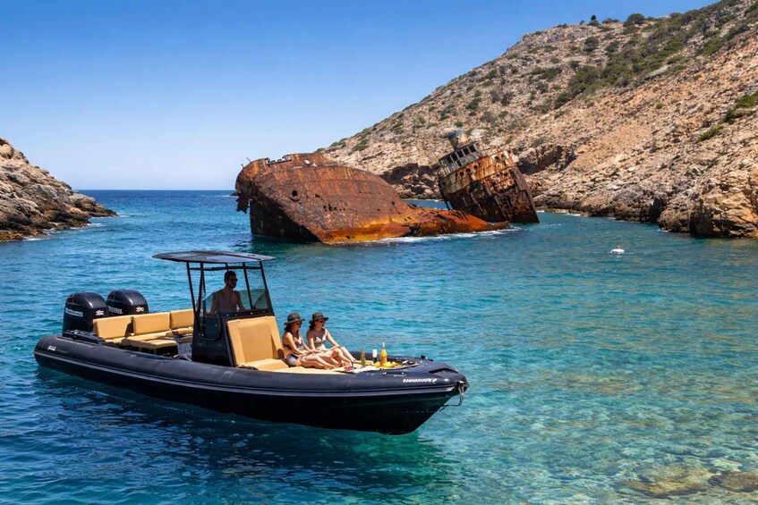 A boat with two people and a driver, a rusty shipwreck, and rocky terrain in clear waters. 5