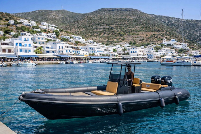 A black inflatable boat docked at a harbor with white buildings and a hill in the background. 2