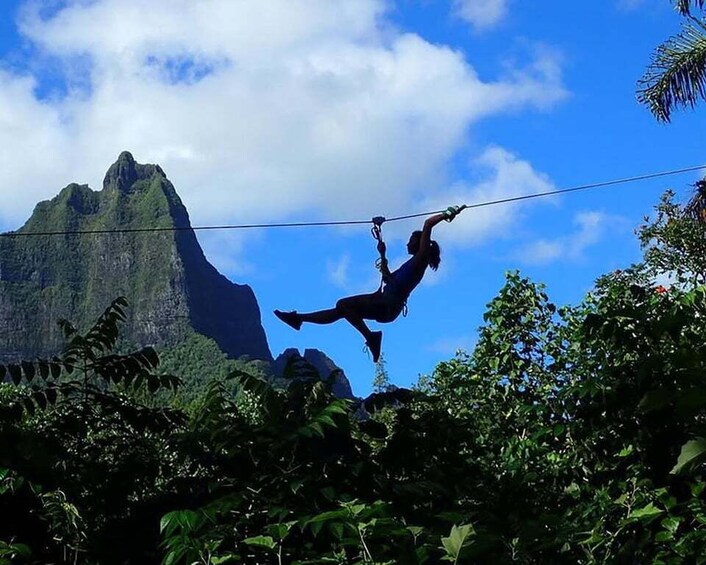 A person zip-lining through a forest with a mountain in the background. 5