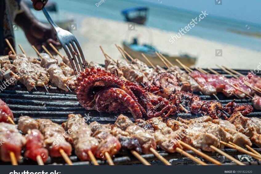 Skewers of meat and seafood grilling on a beach. 4