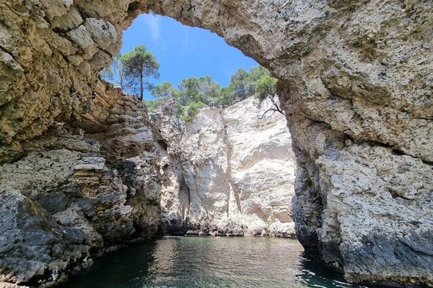 A natural rock arch formation with a clear blue sky and a body of water at its base. 5