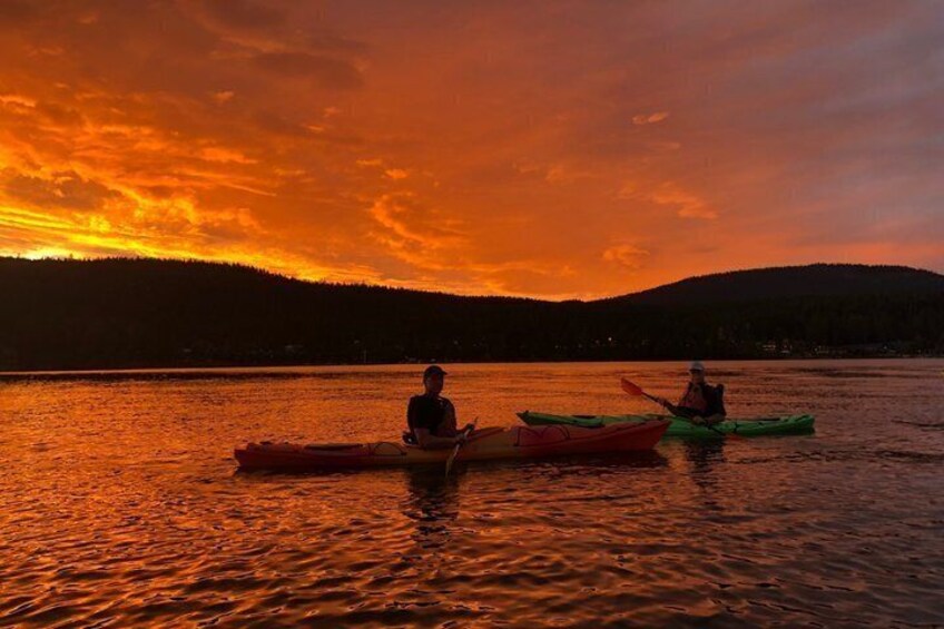 Two kayaks on a calm lake at sunset with a forested hill in the background. 2