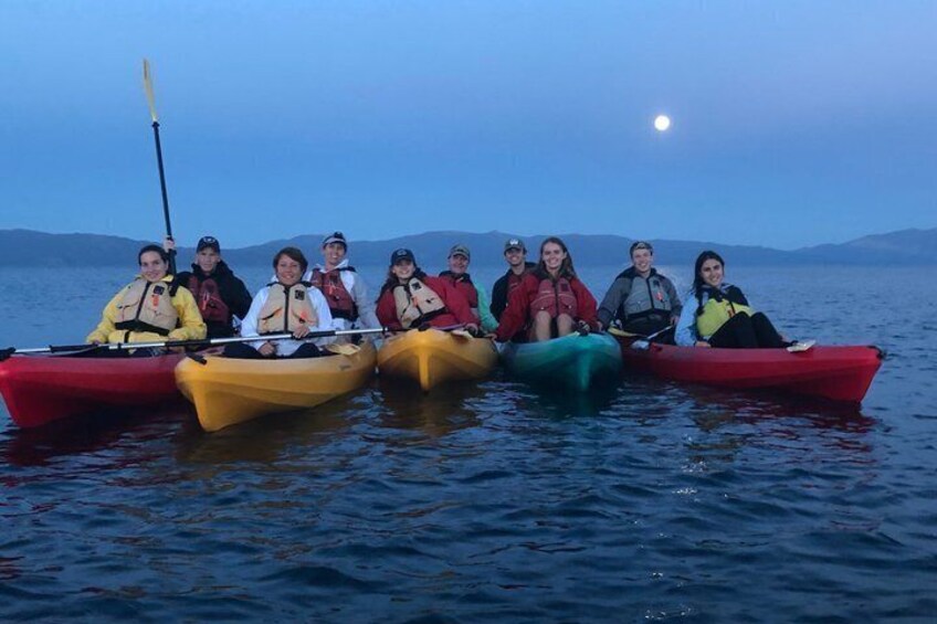 A group of people in colorful kayaks on a calm body of water at dusk. 1