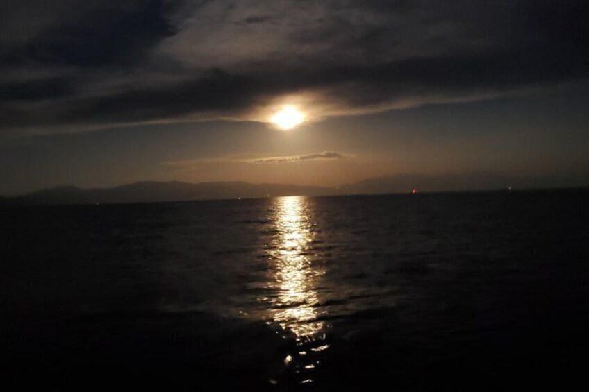 A sunset over a calm sea with a visible horizon and distant mountains. 3