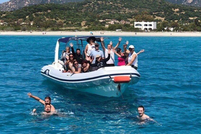 A boat with people on it, surrounded by clear blue water and a beach with buildings in the background. 1
