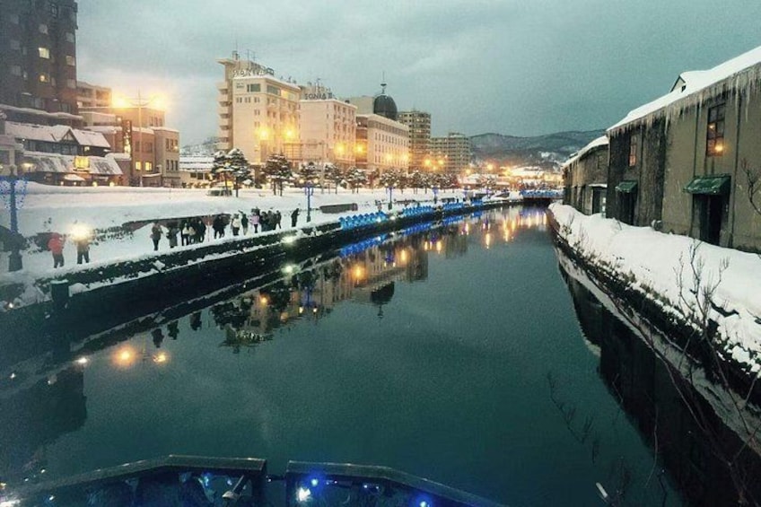 A snow-covered canal with buildings and lights reflecting on the water. 1