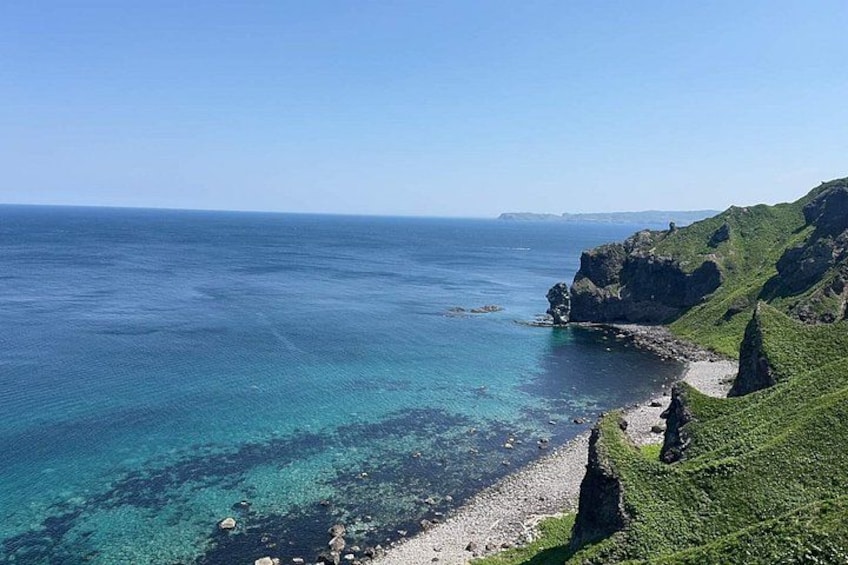 A coastal landscape with clear turquoise waters, rocky cliffs, and lush greenery. 3