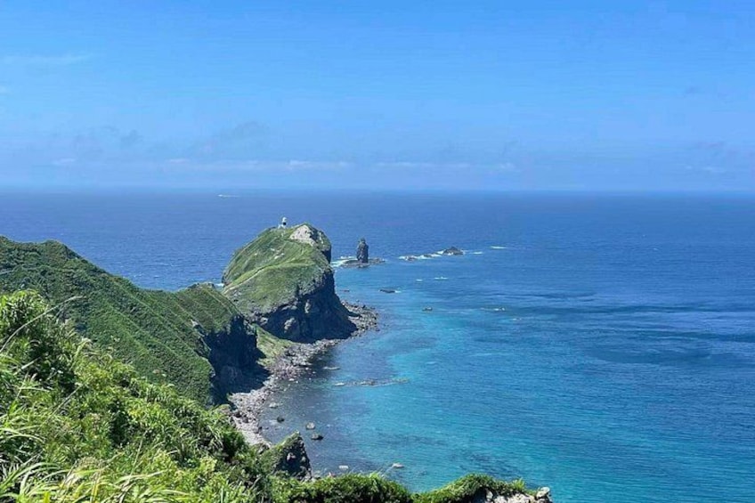 A coastal landscape with a prominent rock formation, clear blue waters, and lush greenery. 5