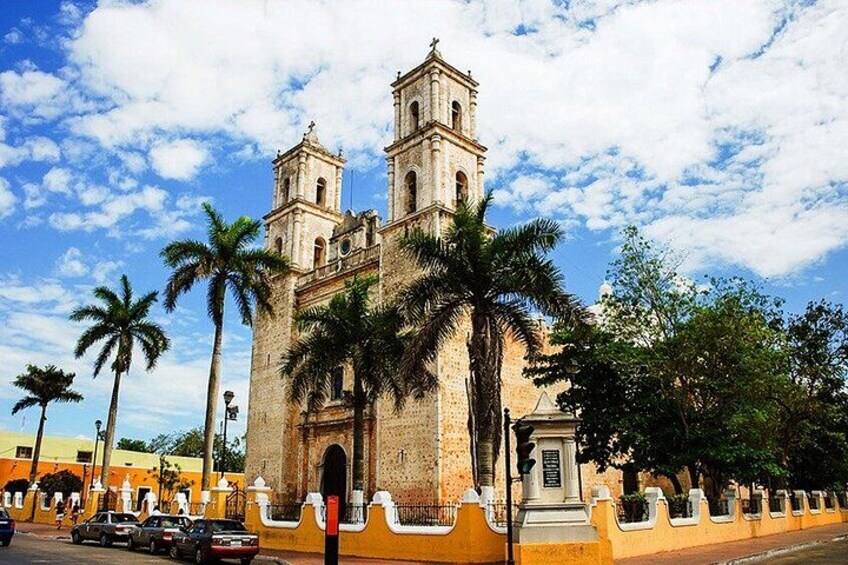 A historic church with two towers, palm trees, and a yellow wall. 2