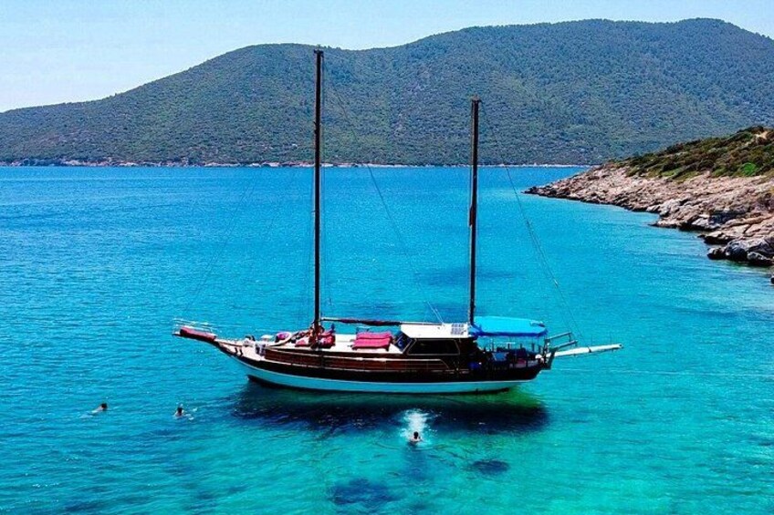 A boat anchored in clear turquoise waters with a mountainous backdrop. 1