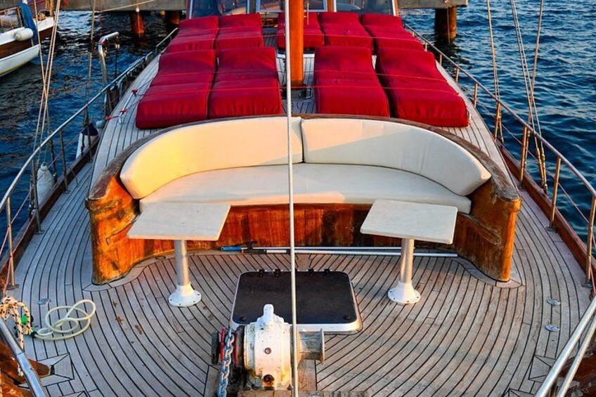 A boat deck with a curved white sofa, red cushions, and a small table. 2
