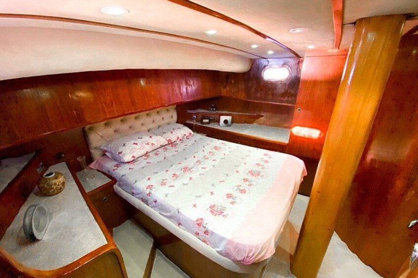 A compact, well-lit cabin with a bed, wooden cabinetry, and a small table with a cup and saucer. 4