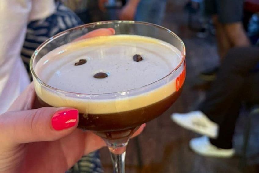 A person holding a cocktail glass with a layered drink and a few chocolate chips. 2