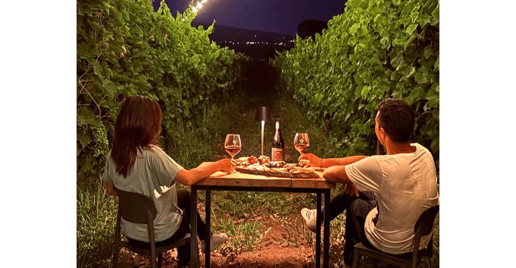 Two people dining at a table in a vineyard at night. 2