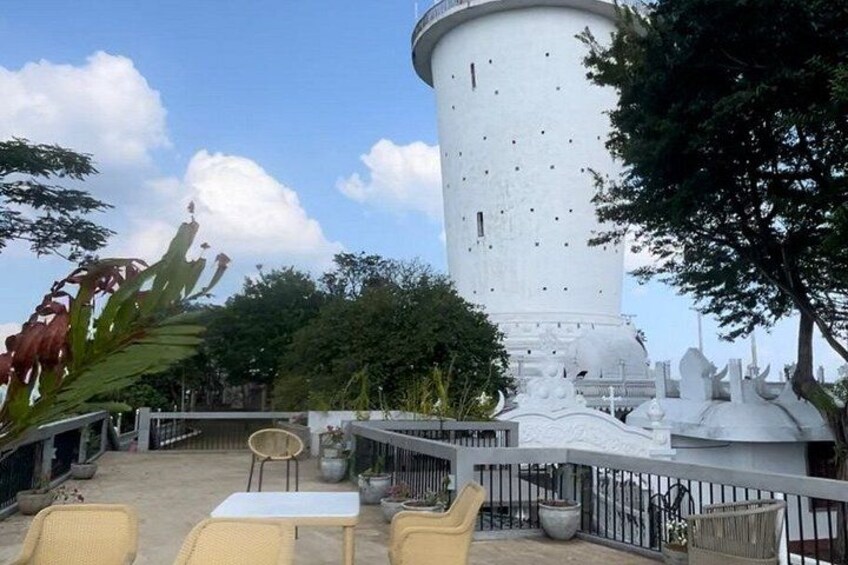 A white cylindrical structure with a balcony, surrounded by greenery and potted plants. 2