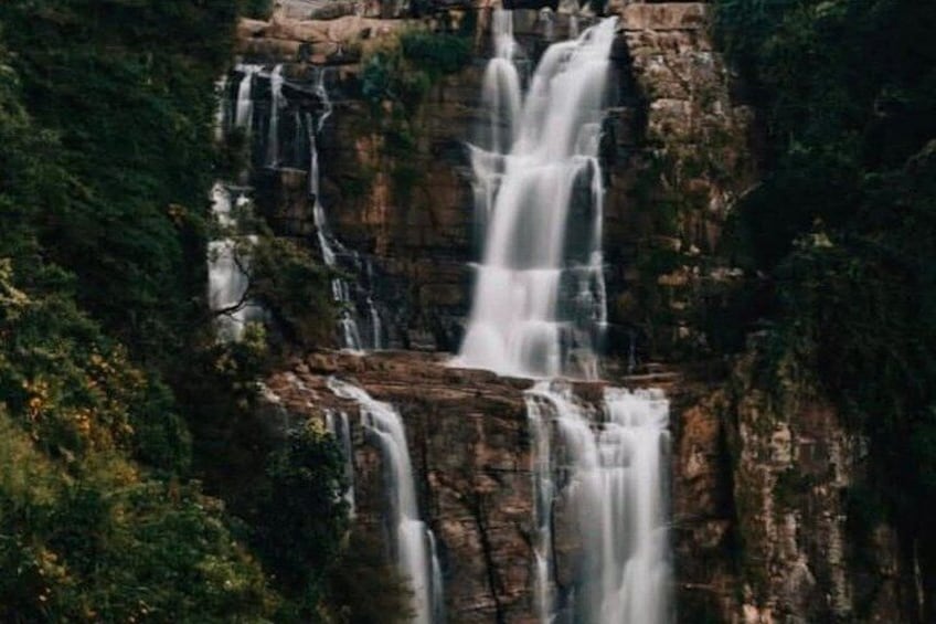 A multi-tiered waterfall cascading down a rocky cliff surrounded by dense greenery. 5