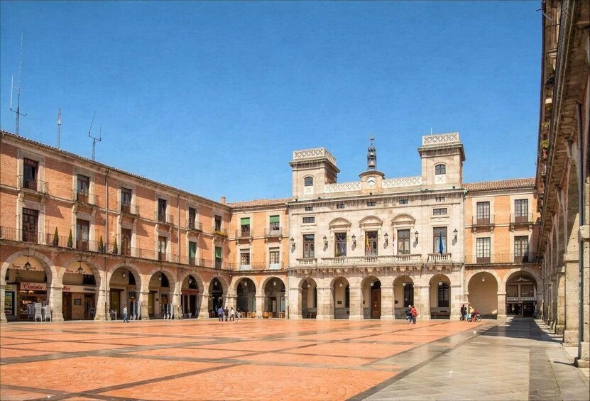 A historic courtyard with a central building featuring arches and a tiled floor. 2