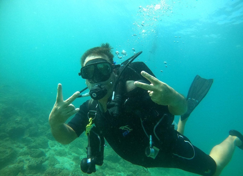 A person scuba diving underwater, making a peace sign with their hand. 5