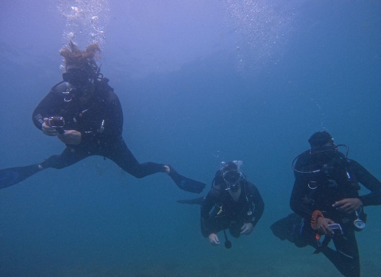 Three scuba divers underwater, each with a regulator and fins. 2