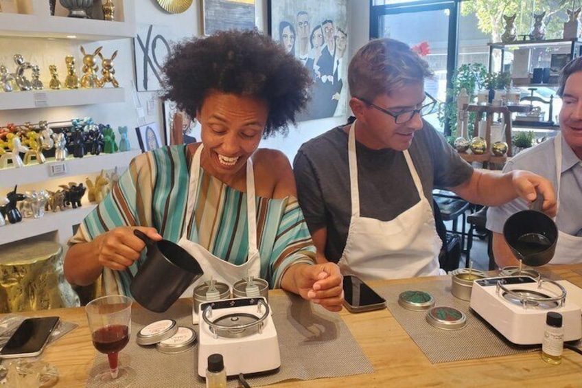 A person pouring liquid into a container, another person holding a black object, and a third person with a smartphone on the table. 4