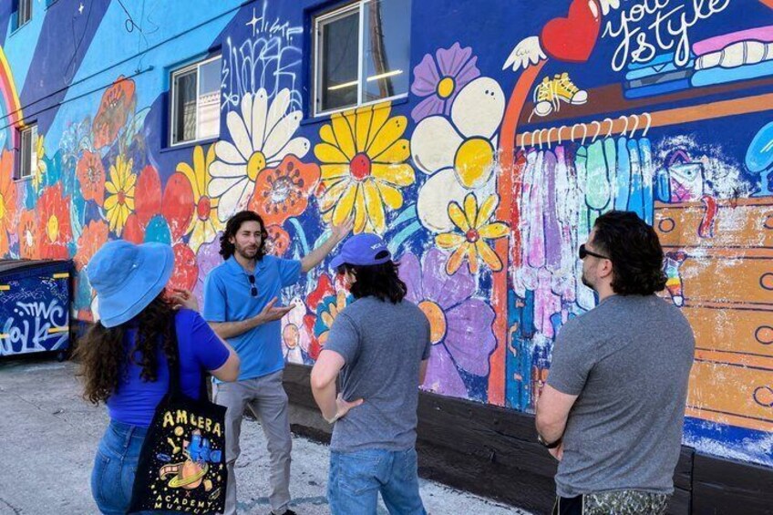 A group of people standing in front of a colorful mural with floral patterns and text. 1