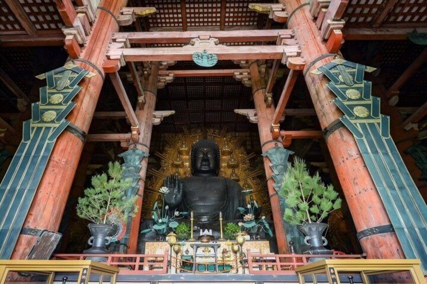 A large black statue in a temple with red and green pillars and a golden background. 1