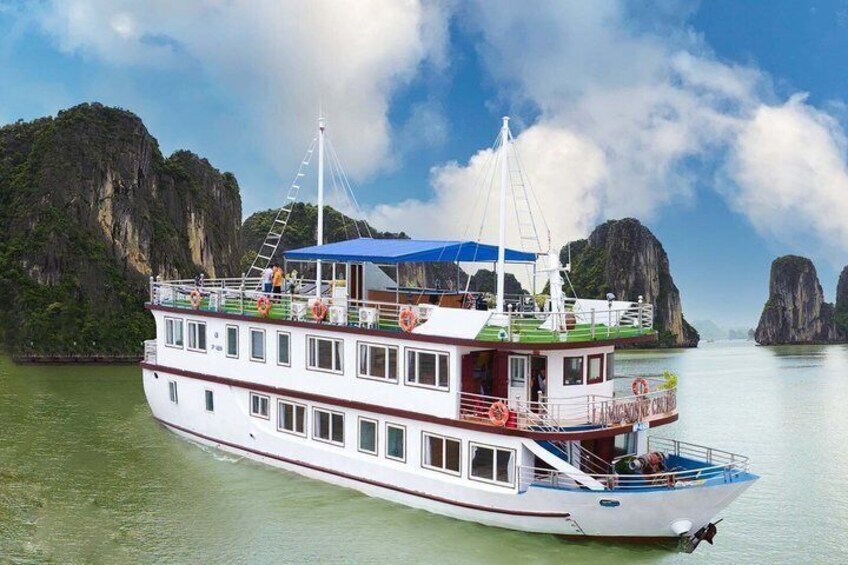 A large white boat with a blue canopy, white railings, and a red deck, floating on calm water with a mountainous landscape in the background. 3