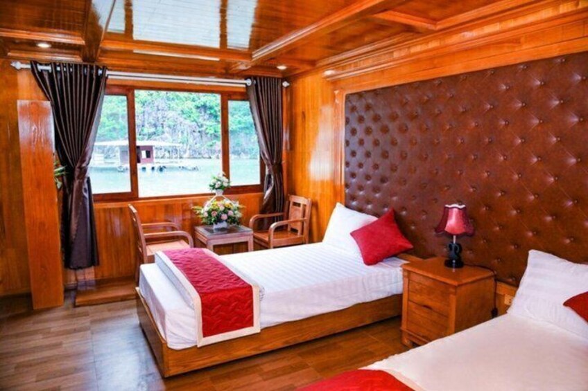 A wooden cabin bedroom with a large bed, two chairs, a nightstand, and a window overlooking a natural landscape. 5