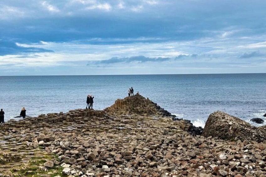 A rocky coastal area with people walking and standing on a stone structure by the sea. 1