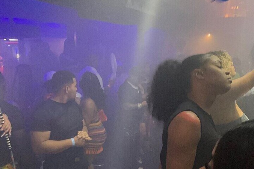 A crowded indoor event with people dancing and a DJ booth in the background. 4