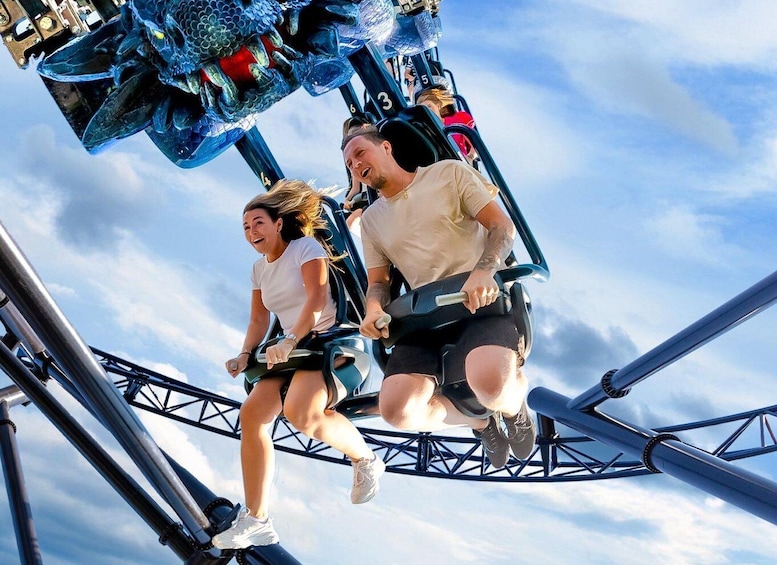 Two people on a roller coaster, holding onto the bars, with a clear sky in the background. 1