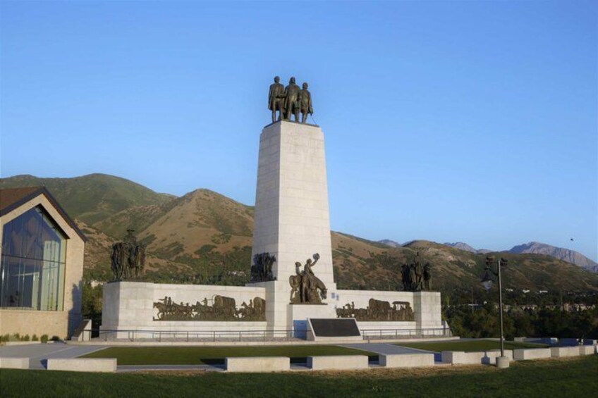 A monument with statues, a building with a glass facade, and mountains in the background. 4