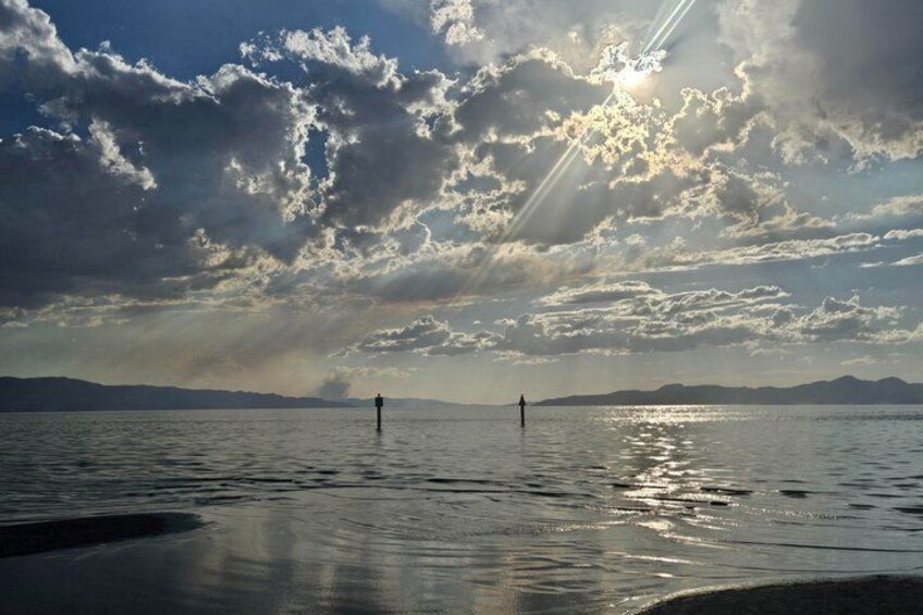 A calm lake with two people standing in the water, surrounded by mountains and a cloudy sky. 3