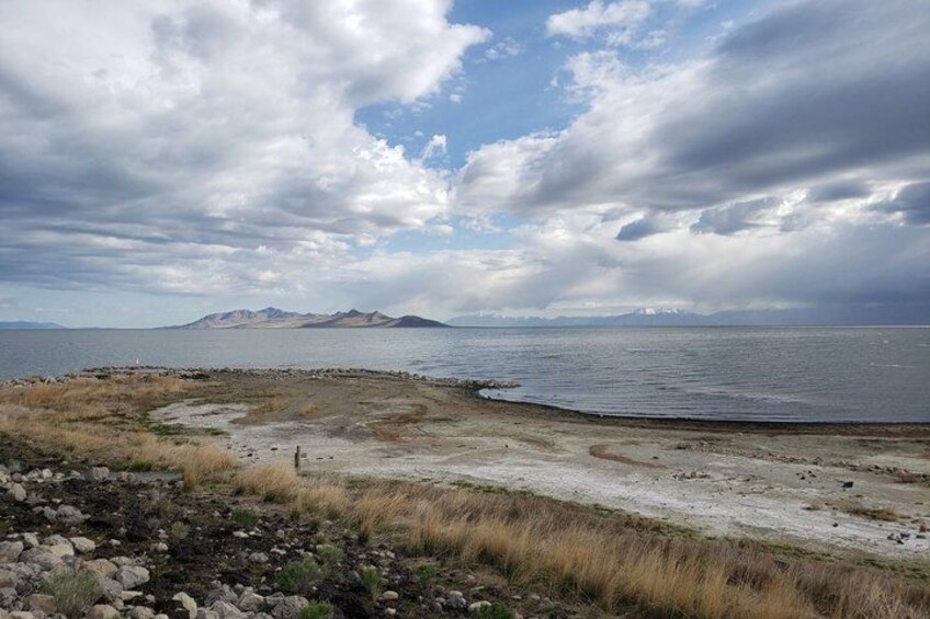 A coastal landscape with a rocky shoreline, a sandy beach, and distant mountains under a cloudy sky. 2