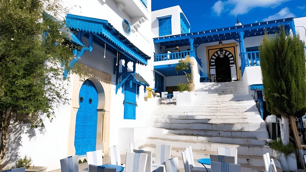Un bâtiment blanc agrémenté de touches de bleu, un escalier menant à un balcon et des sièges installés à l’extérieur. 2