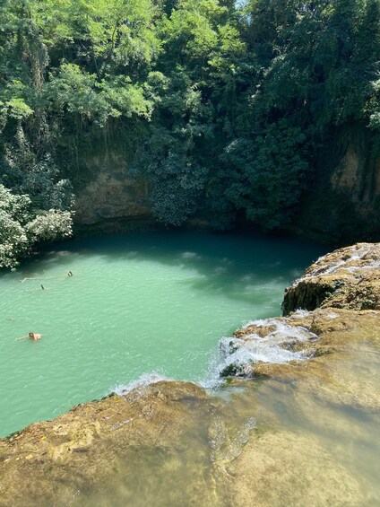 A clear turquoise pool surrounded by lush greenery and rocky terrain. 2