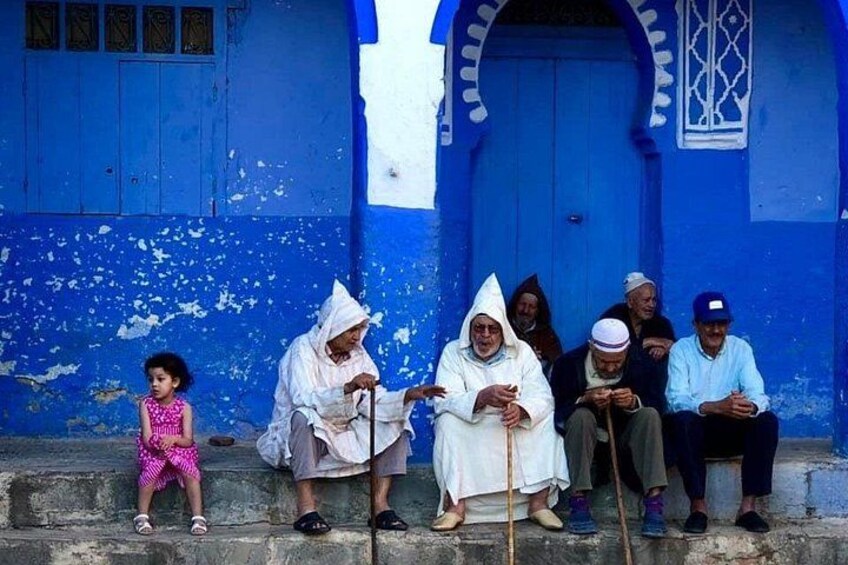 A group of people sitting on steps in front of a blue building with a white door and window. 3