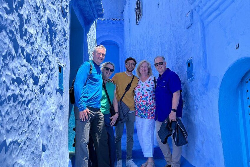 A group of people standing in a narrow alleyway with blue-painted walls and a white door. 2