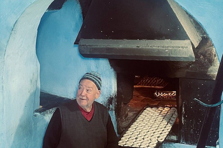 A person standing in front of a brick oven with doughnuts visible inside. 2