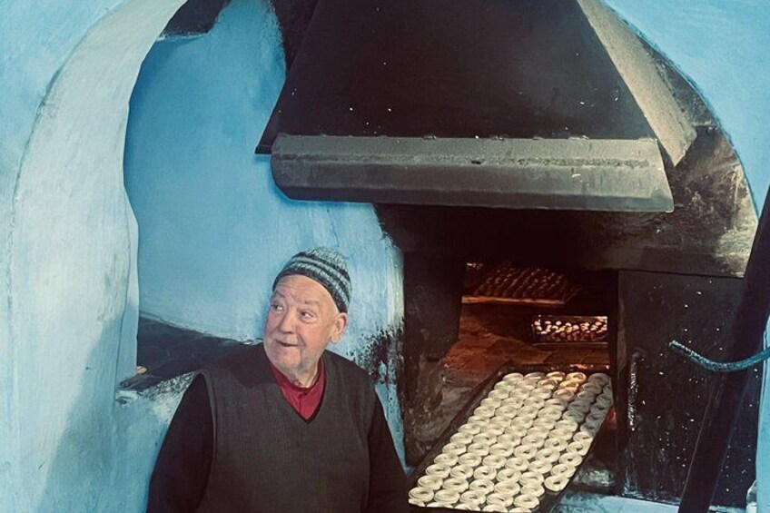 A person standing in front of a traditional wood-fired oven with a tray of bread. 5
