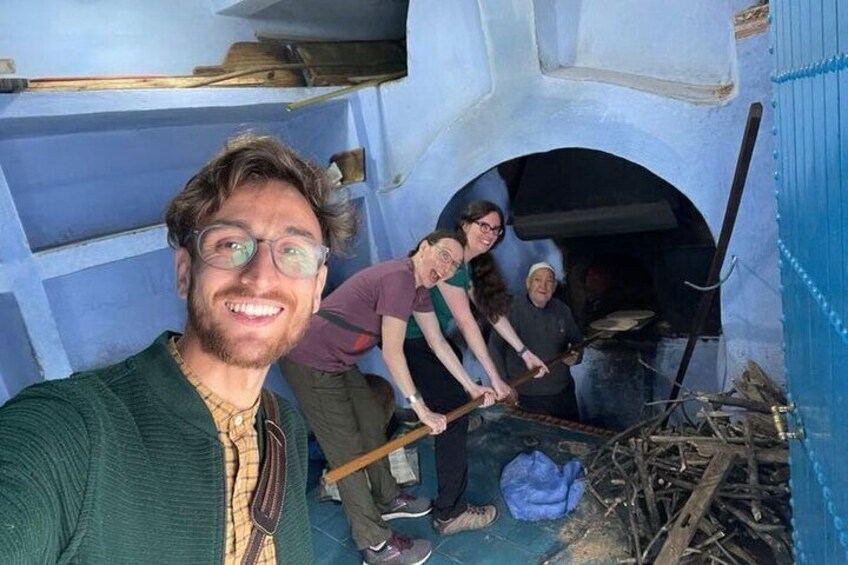A person taking a selfie with a group of people working in a blue-walled building, possibly a workshop or kitchen. 1