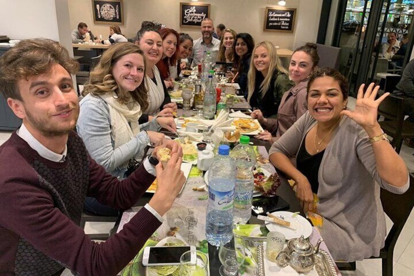 A group of people dining at a restaurant with a long table, plates of food, and water bottles. 2