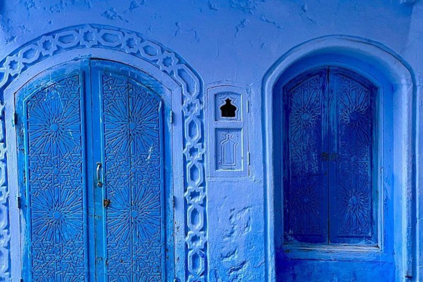 A blue door with intricate patterns, a white arched doorway, and a small window with a decorative frame. 3