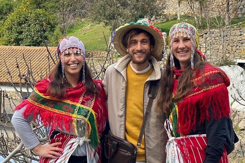 Three people in traditional attire with a stone wall and trees in the background. 5