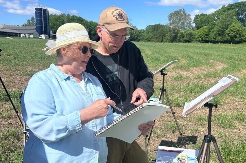 Two people outdoors with a notebook, a tripod, and a music stand. 1