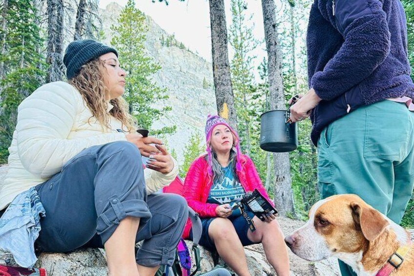 Three people sitting on a rock with a dog, in a forested area. 5