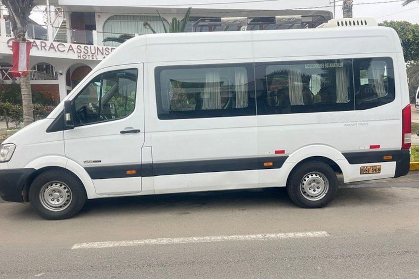 A white van parked on a street with a hotel in the background. 1