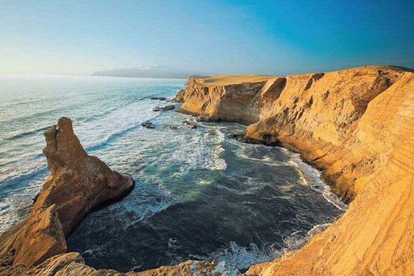 A coastal cliff with a rock formation, ocean waves, and clear sky. 2