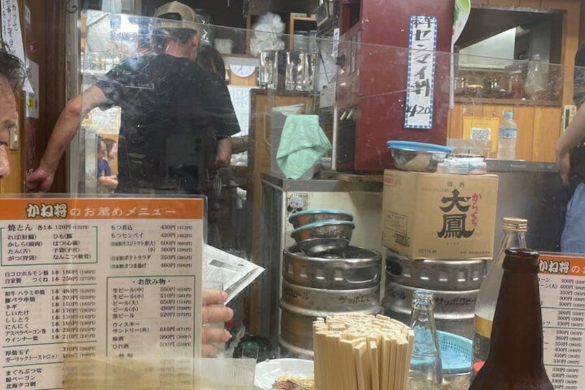 A restaurant interior with a menu board, cooking pots, and a person working behind the counter. 2